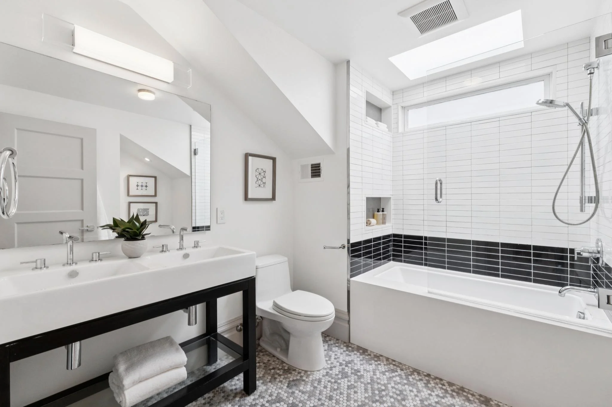 Modern bathroom with white walls, black and white tiled floor, a white sink with a black stand, a large mirror, artwork on the wall, and a walk-in shower with white tiles and a large window.