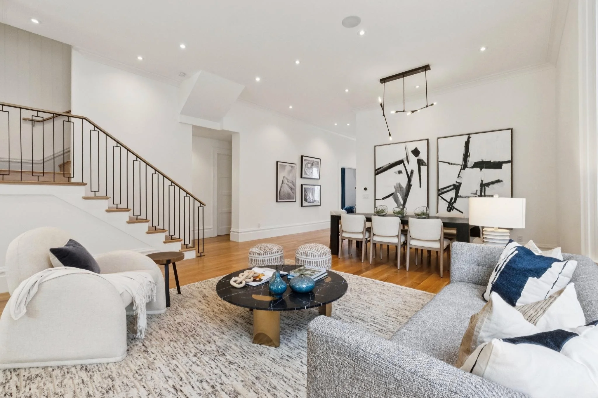 Open-concept living room with white sofas, a black marble coffee table, wood flooring, and modern black and white artwork on the walls.