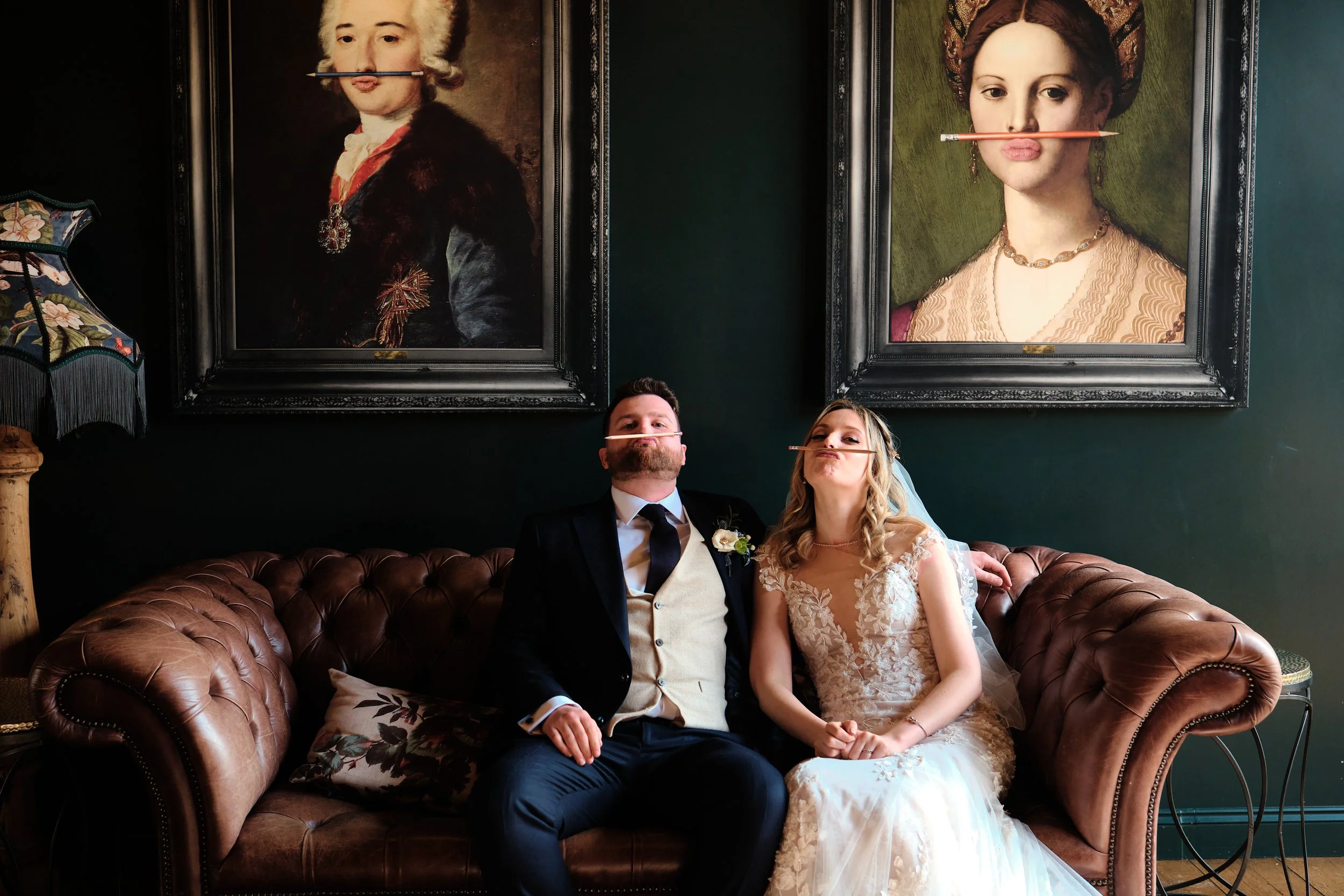 a wedding couple pose for a photograph underneath two paintings at the barns at redcoats Hitchin hertfordshire