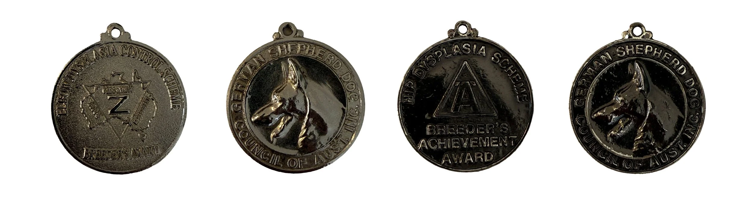 Four black metallic dog awards featuring various engravings and insignias, including a star, a dog's profile, a triangle with an A, and a dog's head, from the German Shepherd Dog Club of the Pacific Southwest.