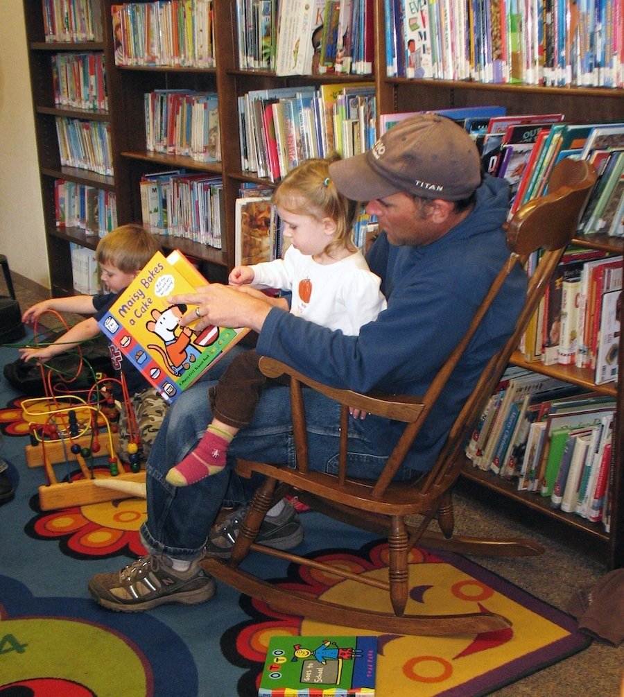 dad reading to child in rocking chair at library