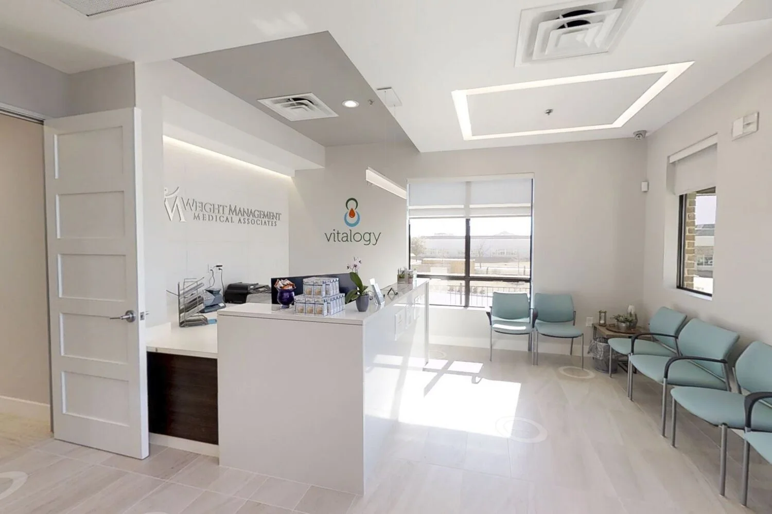 Reception area in a medical office with chairs, a desk, and medical branding on the wall.