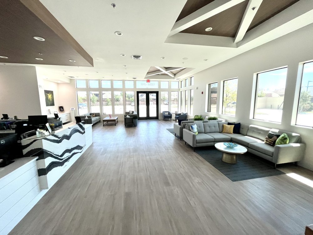 Spacious hotel lobby with a reception desk on the left, large windows allowing natural light, and seating areas with sofas and chairs.