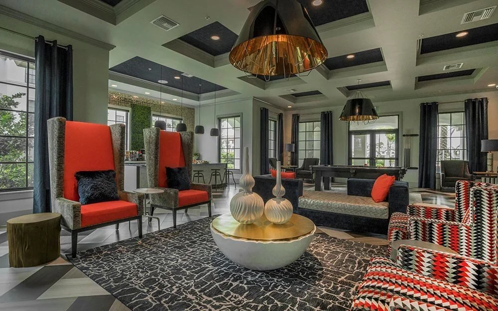Modern living room with black, red, and patterned furniture, large windows with dark curtains, and a mix of decorative objects and lighting fixtures.