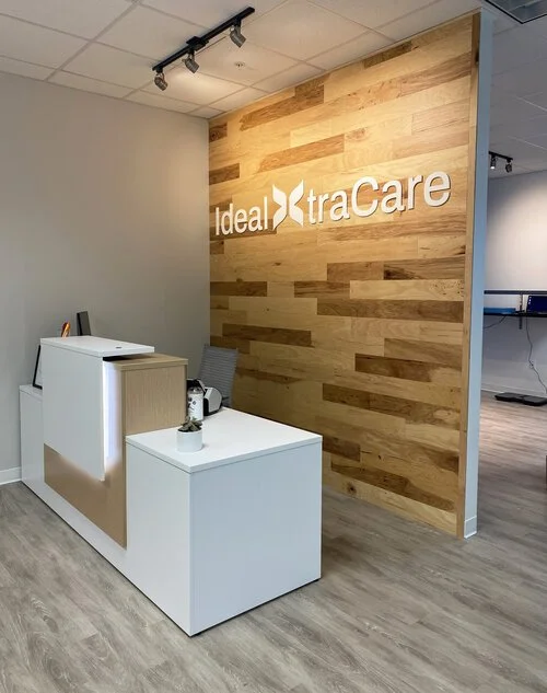 Reception area with a white and beige desk, a chair, and a wood-paneled wall with the 'ideal traCare' logo.