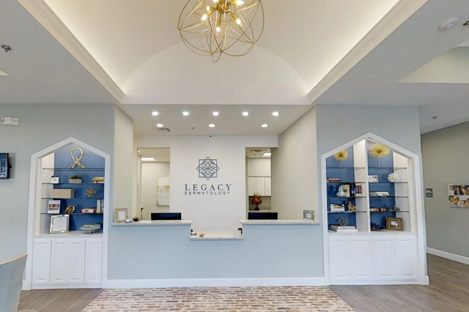 Reception area of Legacy Dermatology with a white front desk, decorative shelves with books and decor, and a wall sign displaying the Legacy Dermatology logo.