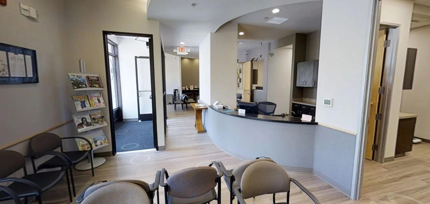 Waiting room with chairs, a magazine rack, a reception desk, and an entrance door.