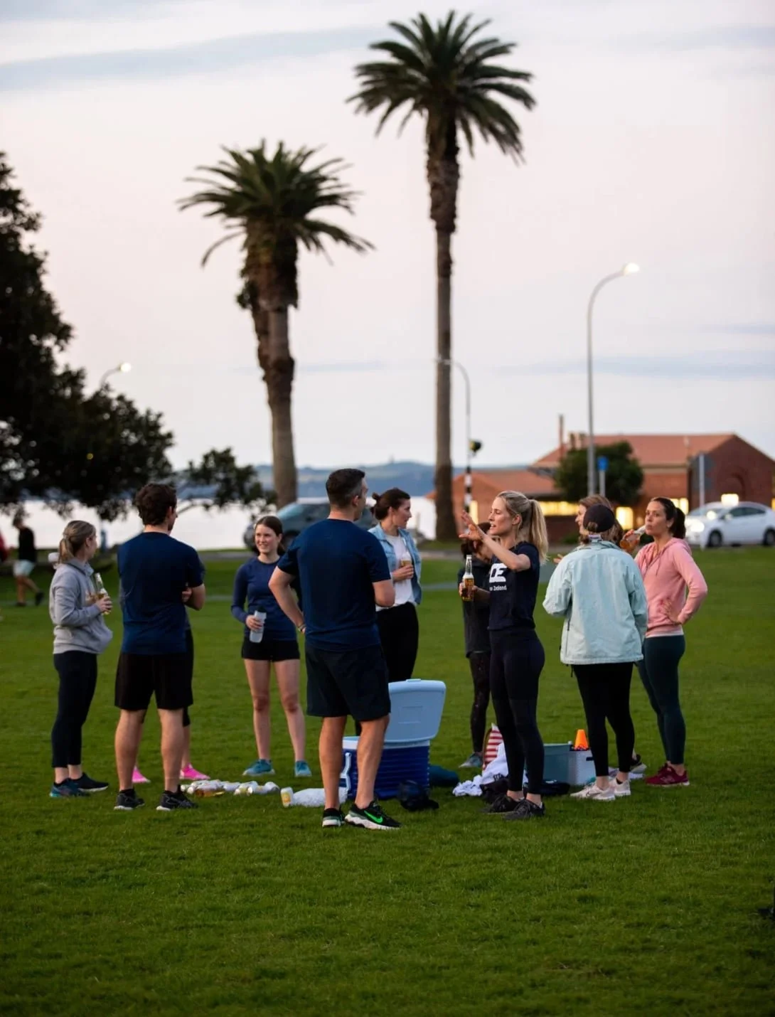 Group of people gathering in St Heliers Auckland at dusk drinking beer after an outdoor group fitness class