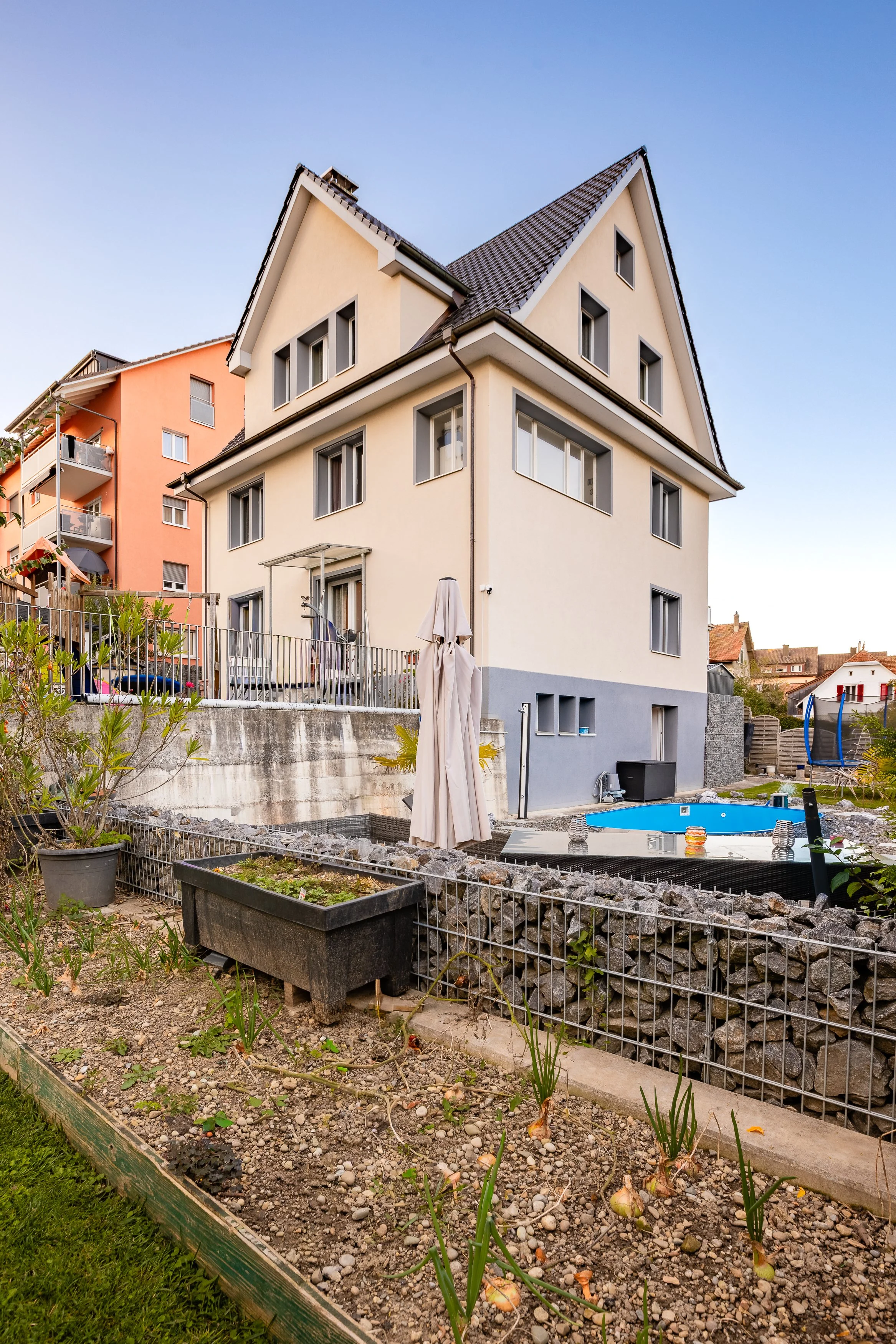 Mehrstöckiges Haus mit Garten und Pool, umgeben von anderen Wohngebäuden bei Sonnenuntergang. Haus in Neuhausen kaufen bei FREITAG IMMO: www.freitagimmo.ch