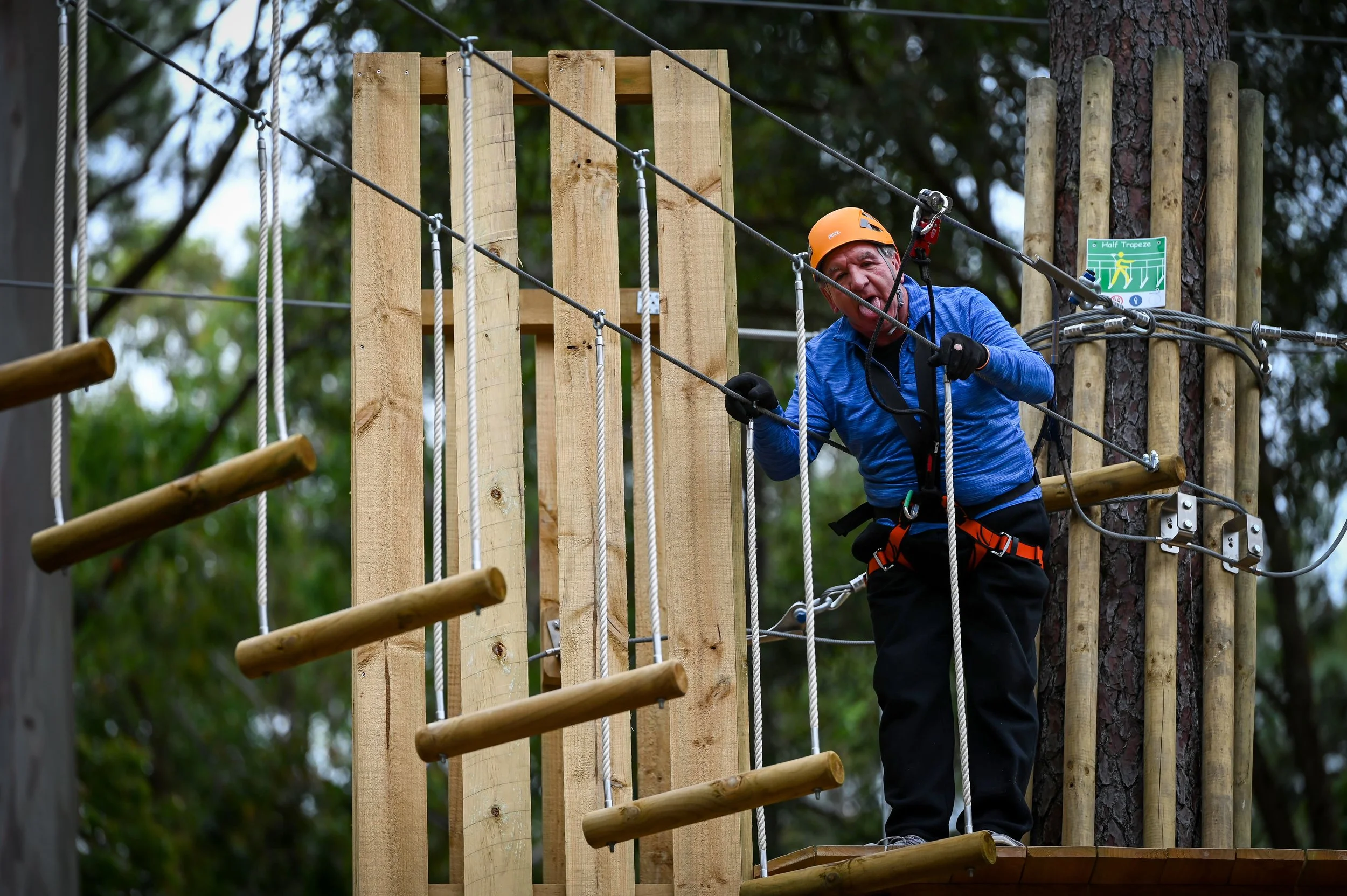 Person in helmet and safety gear on a high ropes course, holding onto ropes and wearing a harness.