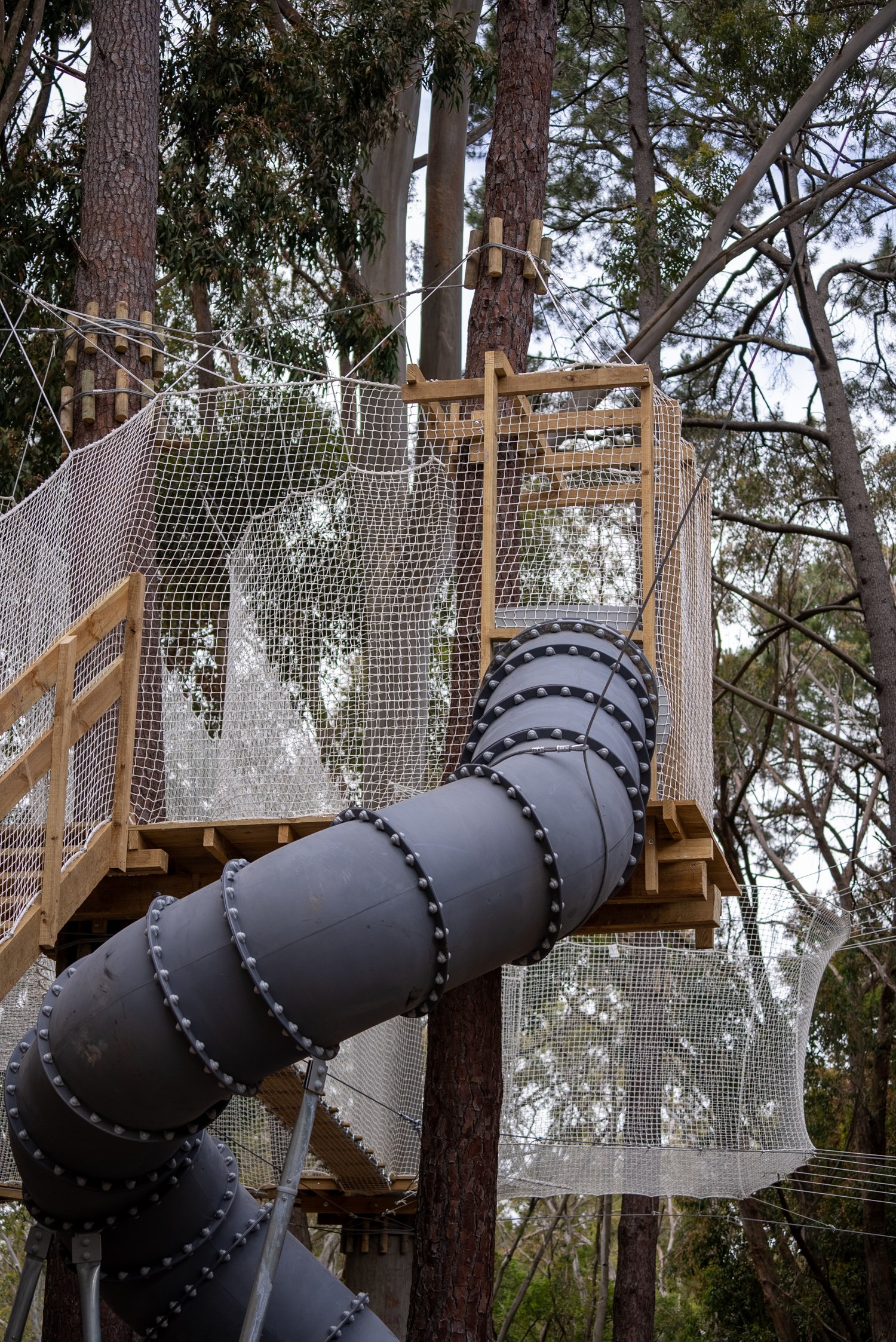 Treehouse with a spiral slide and safety nets in a forest setting.