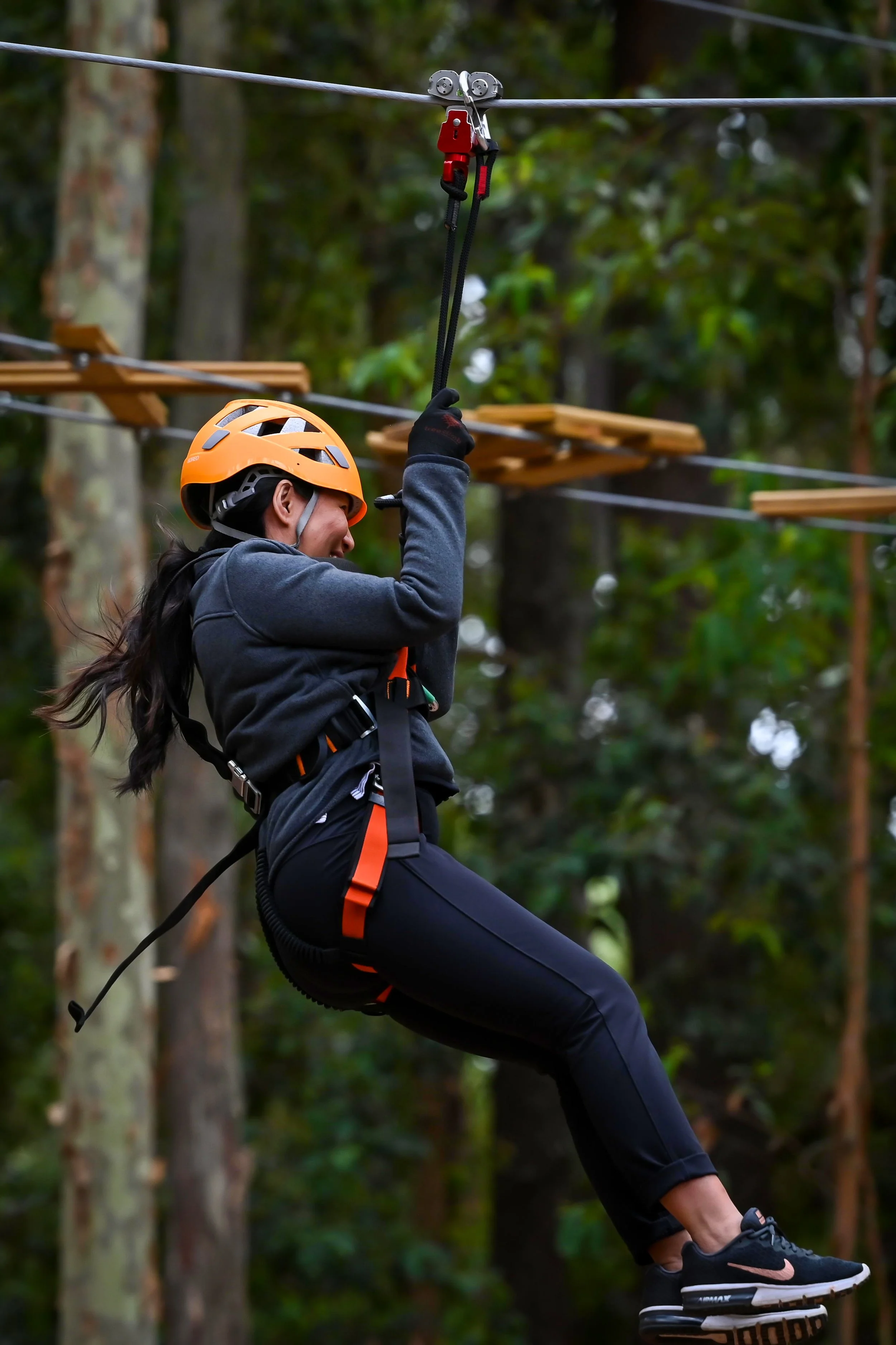 Person zip-lining through a forest wearing an orange helmet and harness.
