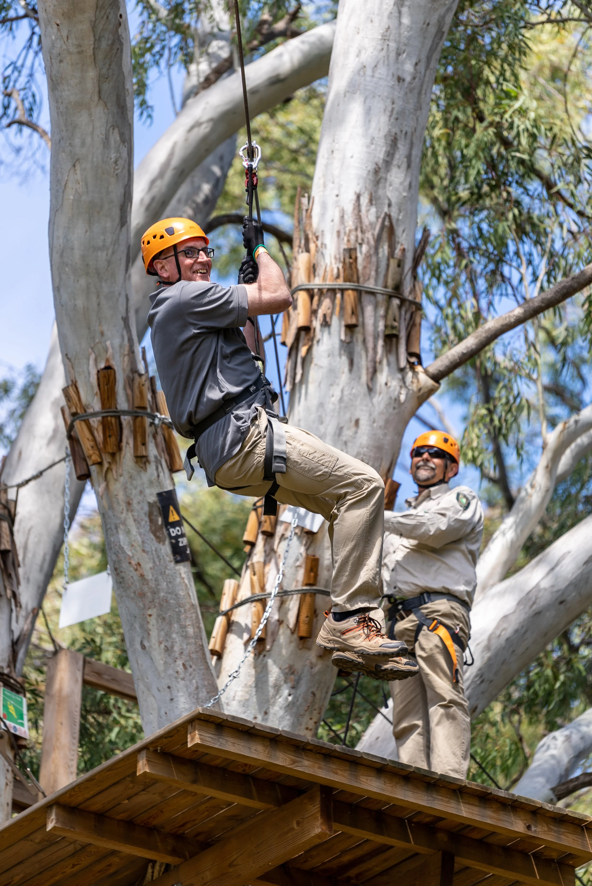Two people in helmets and harnesses enjoy a zip line adventure among trees.