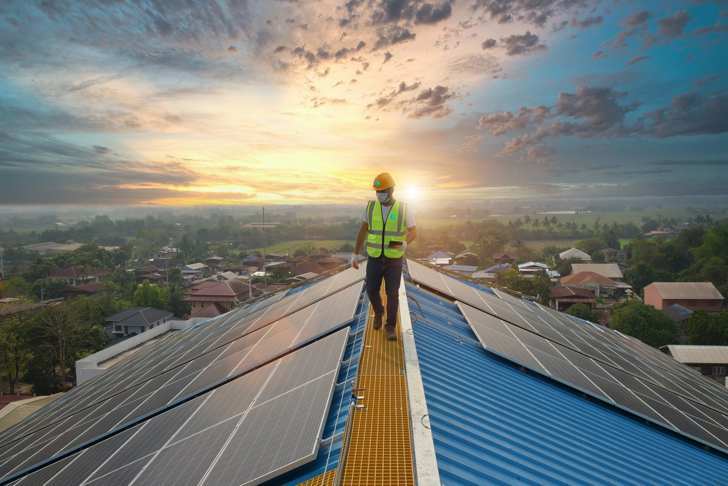 A worker in safety gear walking on a solar panel on a rooftop during sunset.