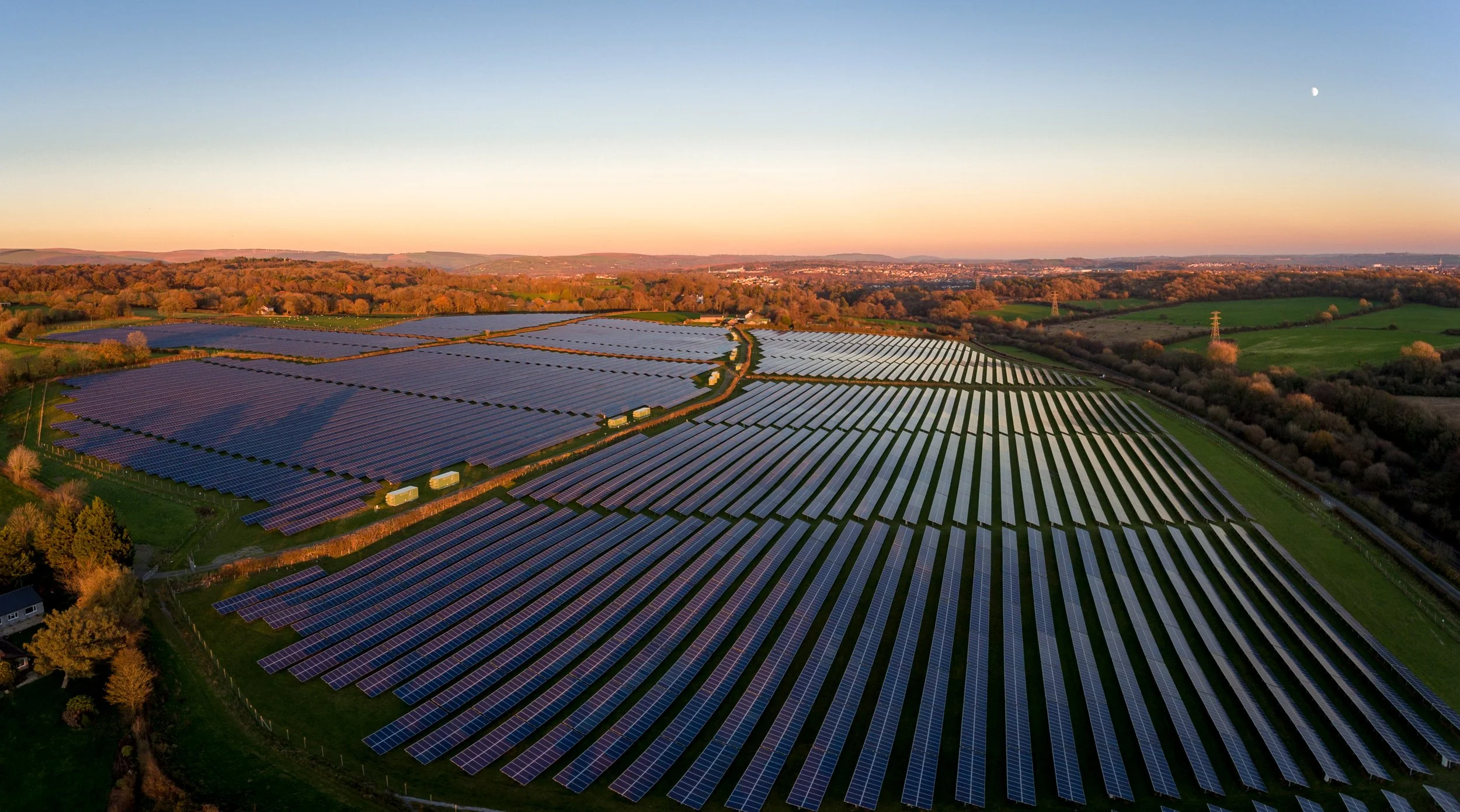 Aerial view of a large solar farm with numerous solar panels on rolling hills during sunset or sunrise.