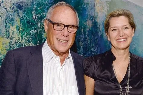 A man in glasses and a woman smiling, standing together in front of a colorful abstract background.