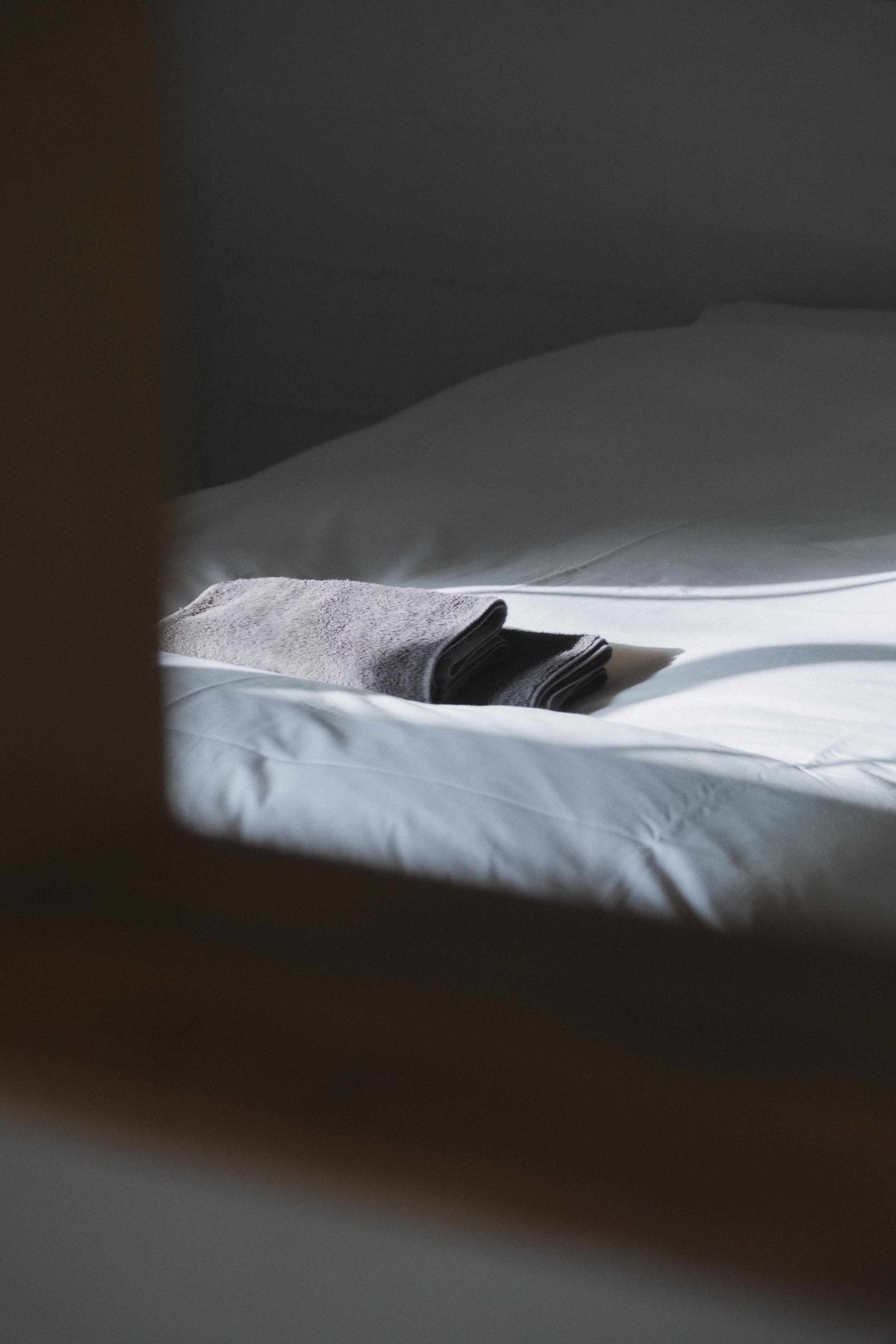 A neatly folded gray towel on a white bed with soft lighting.