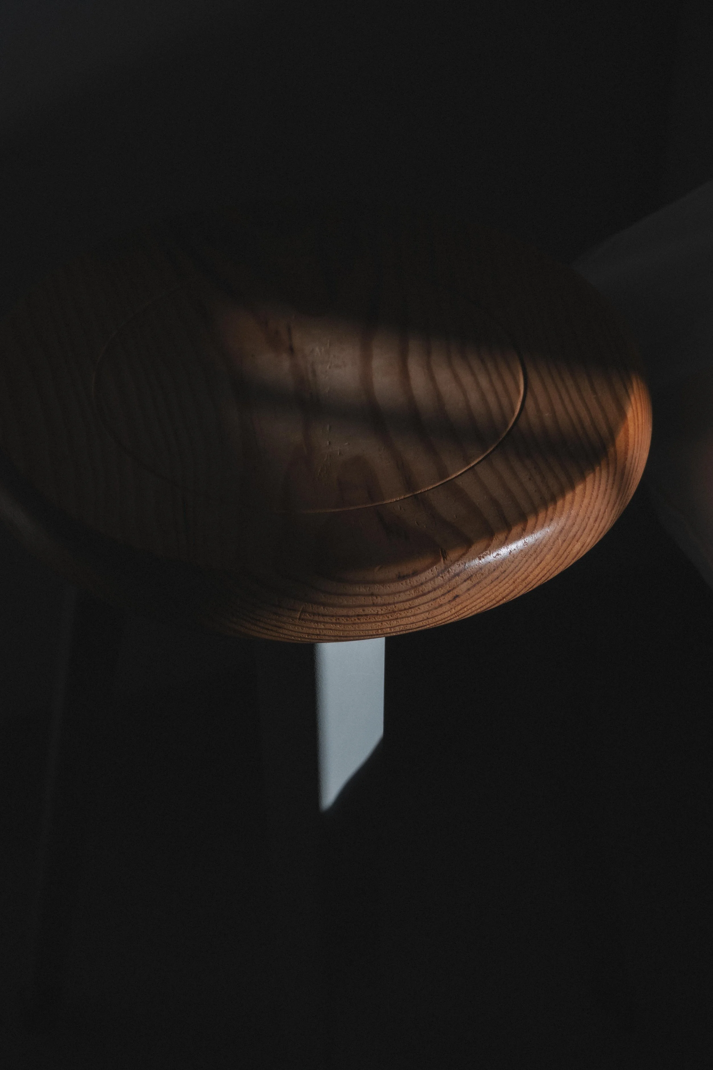 A wooden table with a circular shape, under a shadow in a dimly lit room.