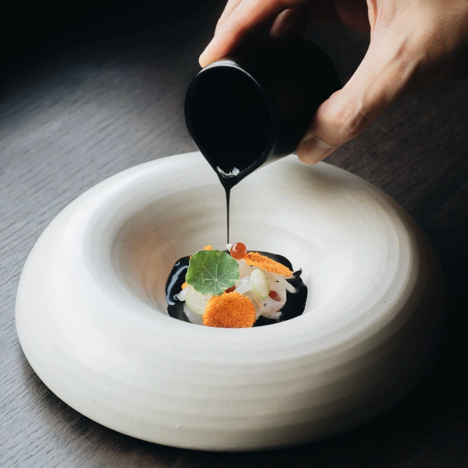 Signature sauce poured over a course in a white ring bowl at Royd