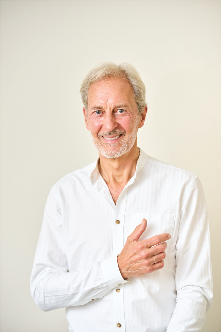 An elderly man with gray hair and a beard smiling, Anthony Thompson, wearing a white button-up shirt, pointing to his left.