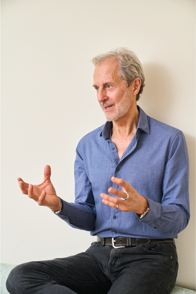 An older man with gray hair and beard, Anthony Thompson, wearing a blue button-up shirt, sitting and gesturing with his hands while talking.