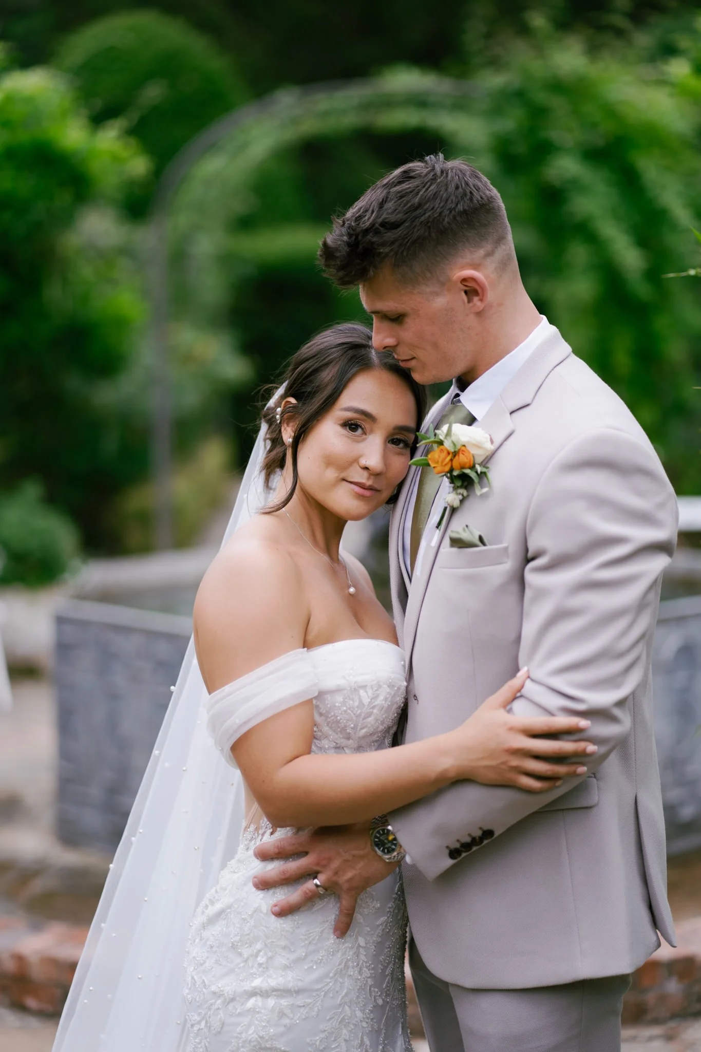 Bride looking at the camera with groom in light coloured suit