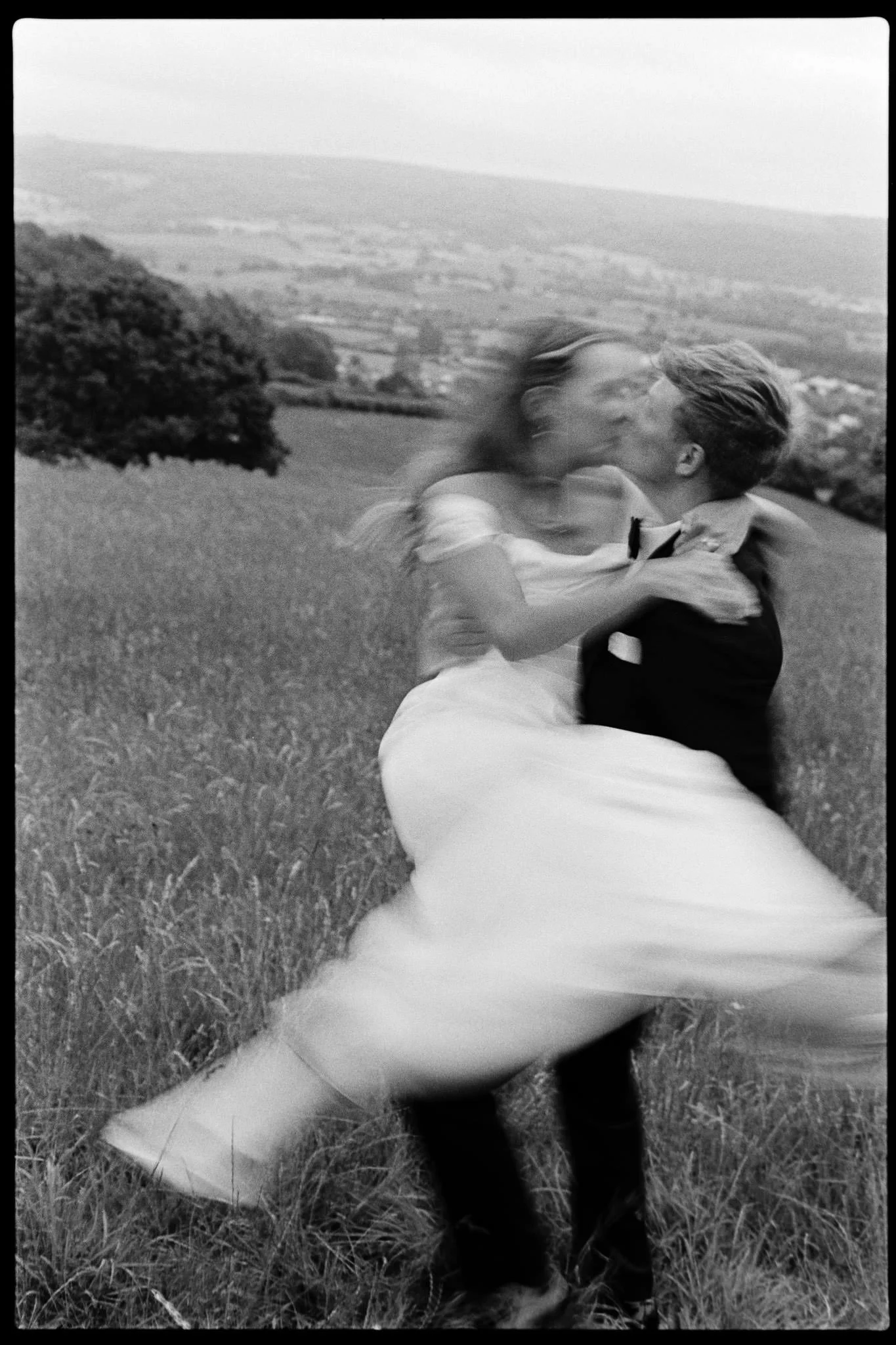 Groom spins bride around in a field outside Bristol at a black tie wedding with shutter drag to give lots of motion.  Shot on black and shite film
