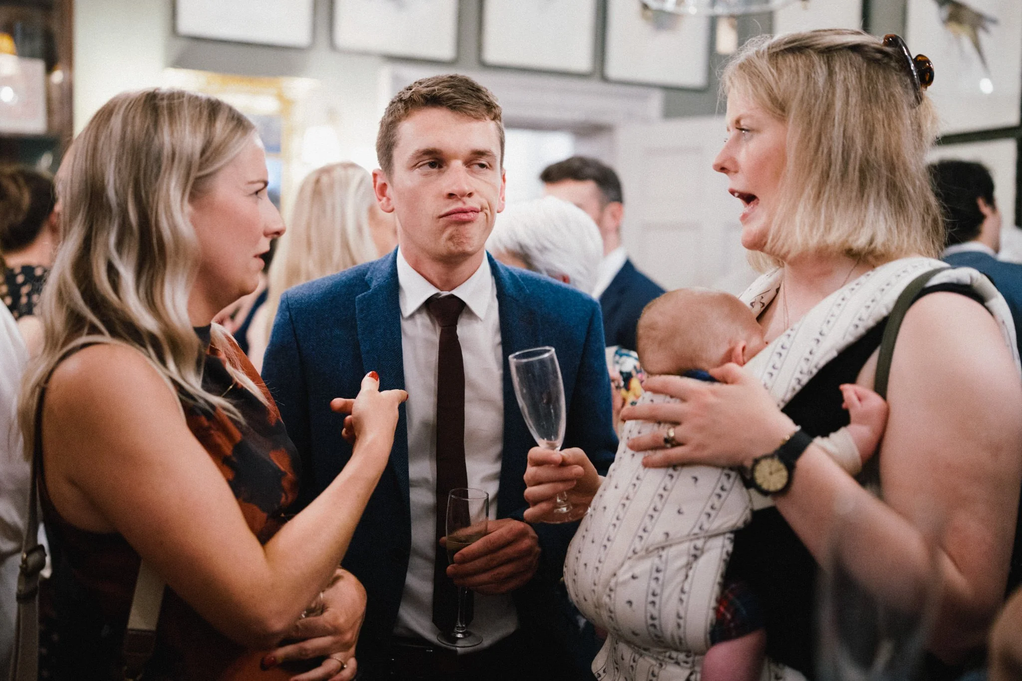 wedding photography of a bored male guest while two women talk about babies