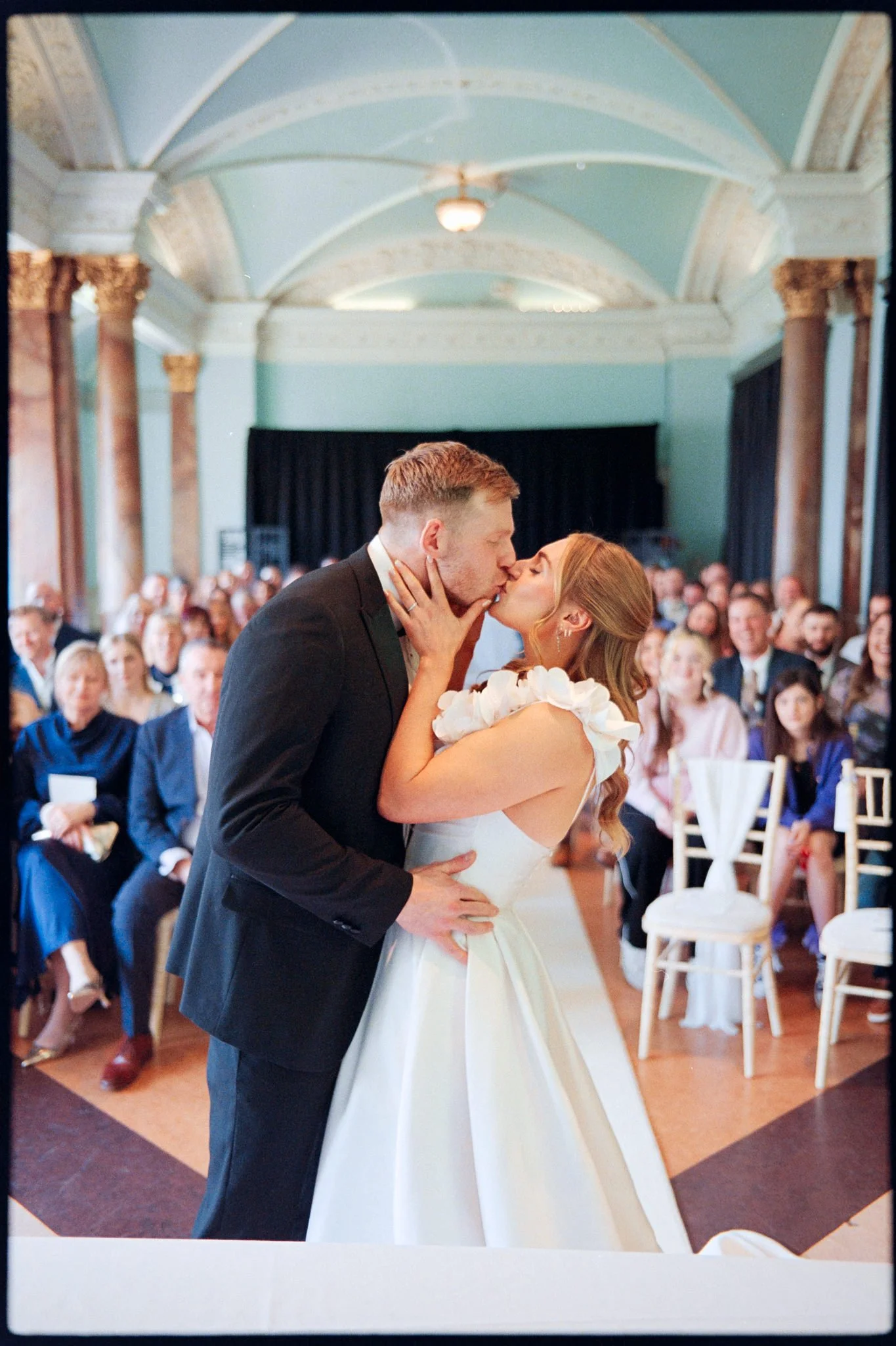A bride and groom sharing a kiss during their wedding ceremony with guests seated in the background.