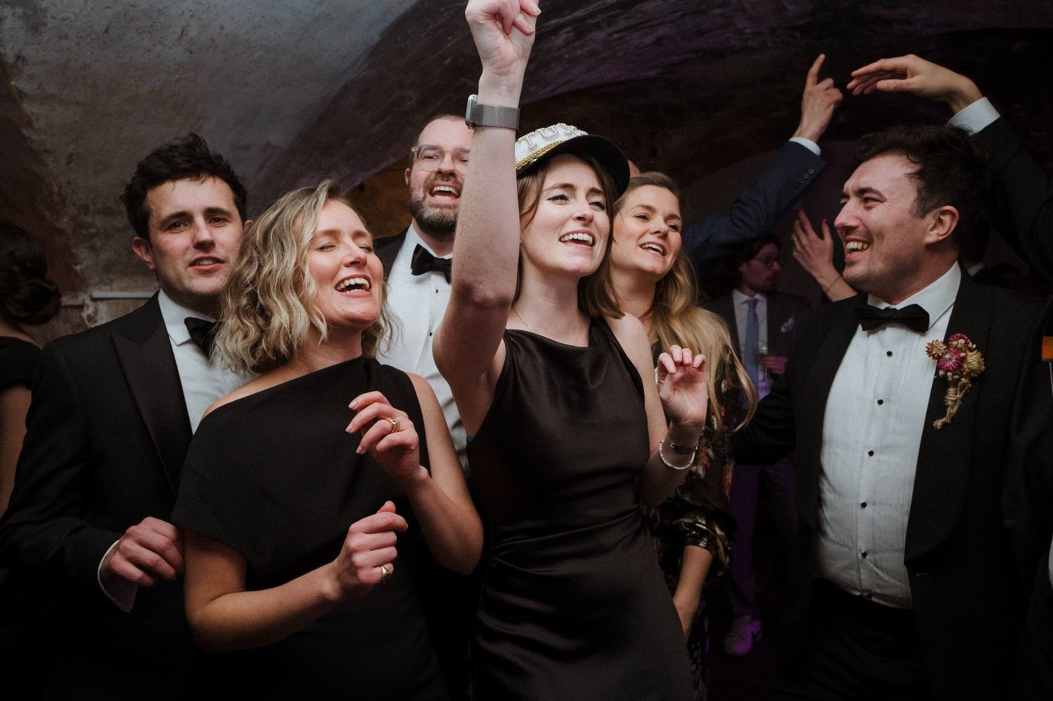 Group of people dancing and celebrating at a formal event, wearing black tuxedos and dresses, smiling and enjoying the moment.