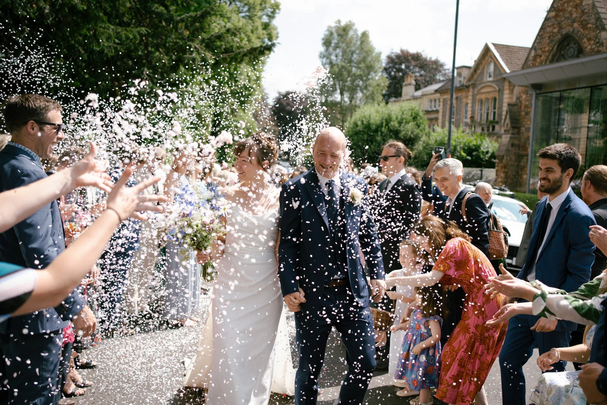 Bride and groom walk through a huge shower of white confetti outside Woodlands Church in Bristol