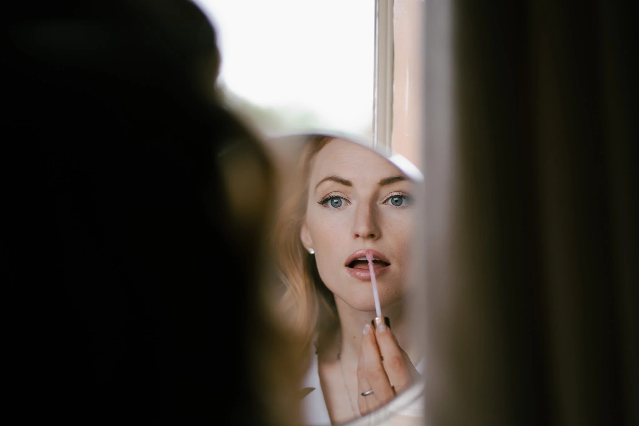 Close up of beautiful bride applying lipstick in a mirror at Dewsall Court