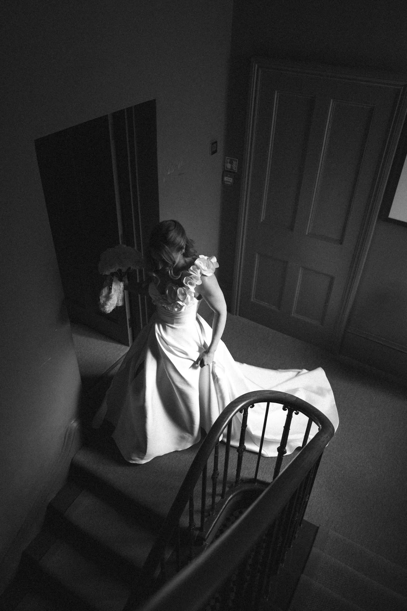 Bride descends the stairs at No 131 Cheltenham with strong window light in black and white, shot on film