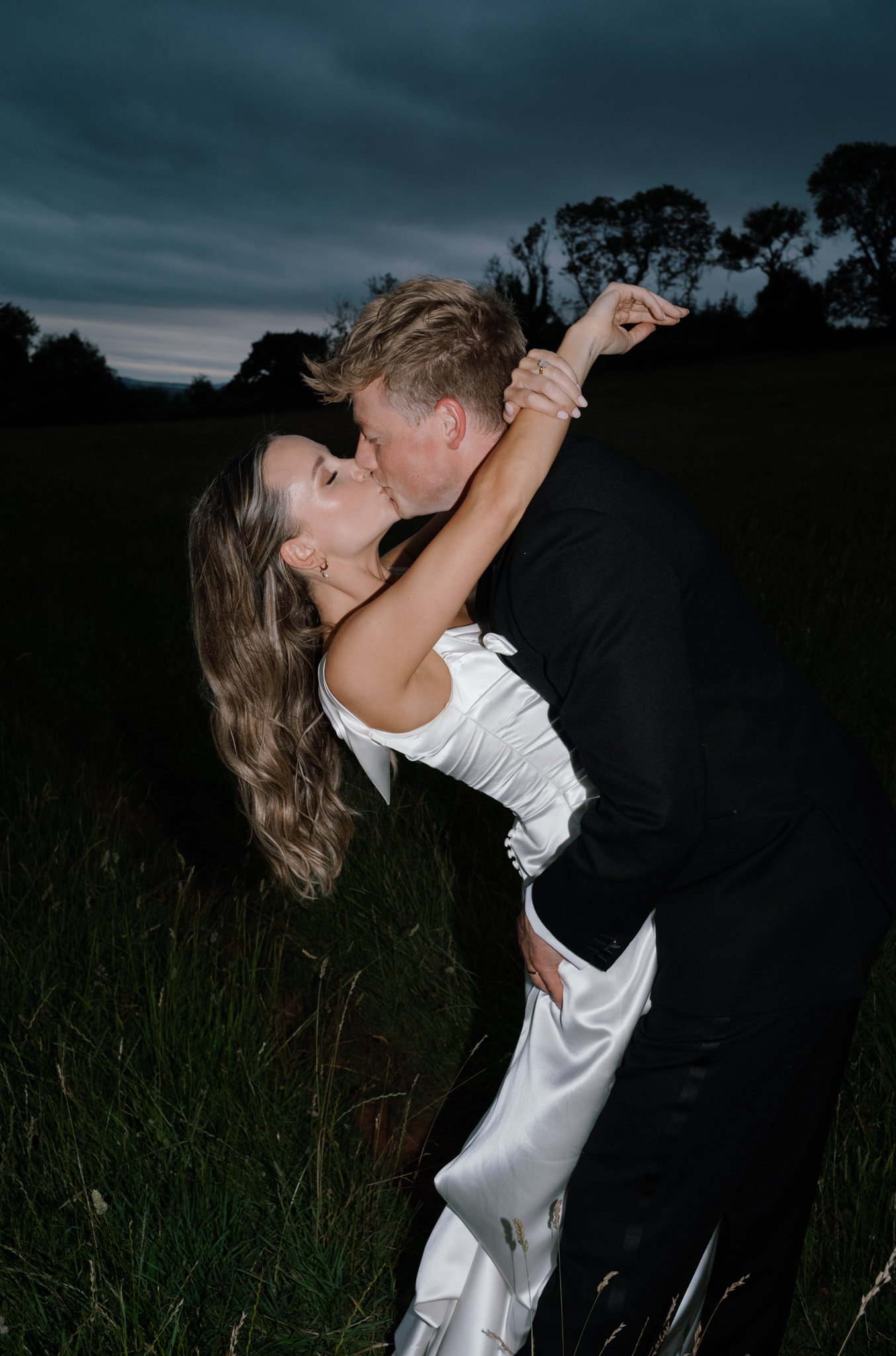 wedding photography of a couple kissing with direct flash in a field