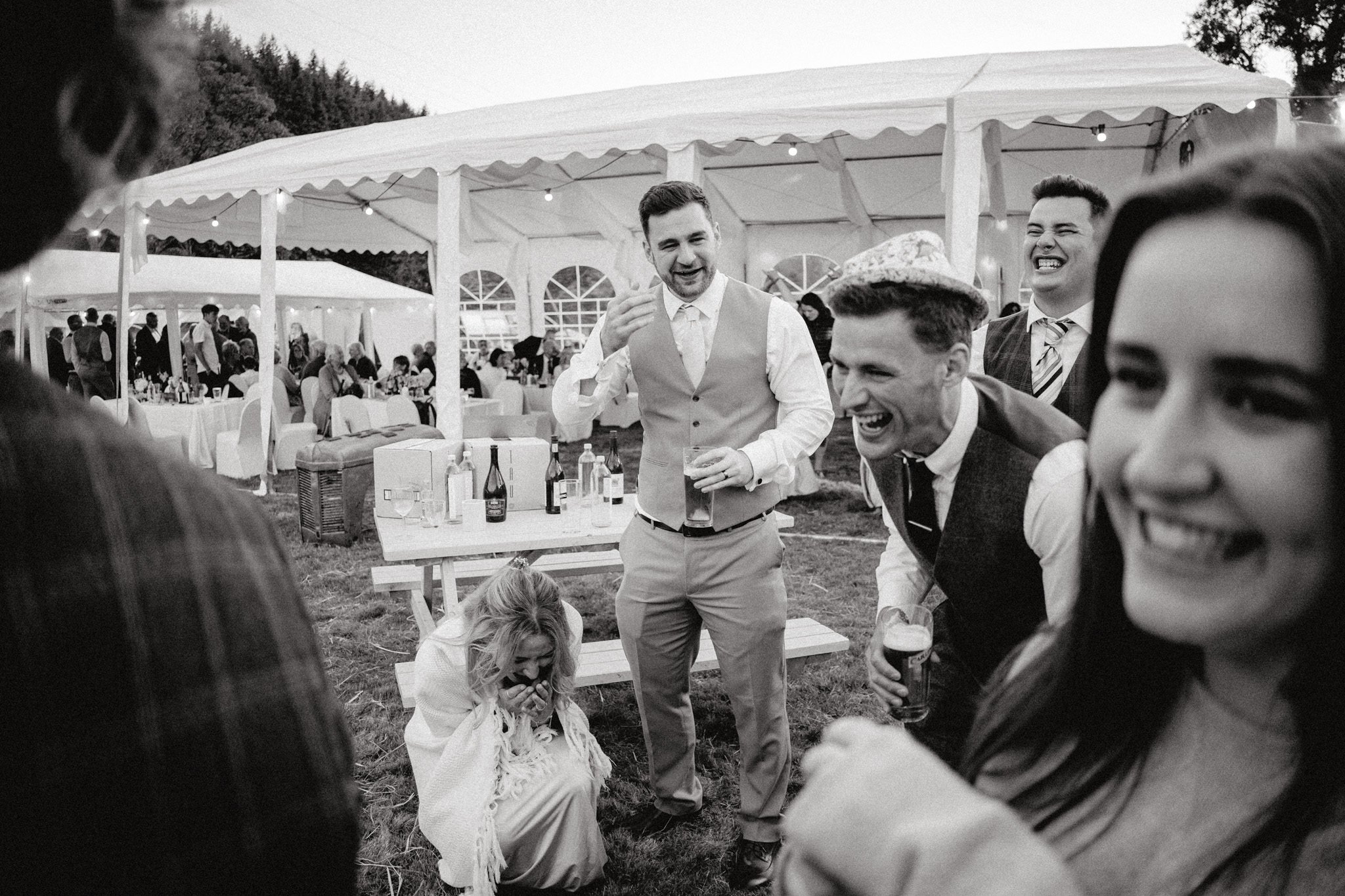 wedding photography of guests breaking down laughing outside a marquee in black and white