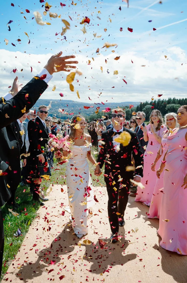 Hand tosses a shower of pink confetti petals across a field near Bristol, a burst of colour and movement