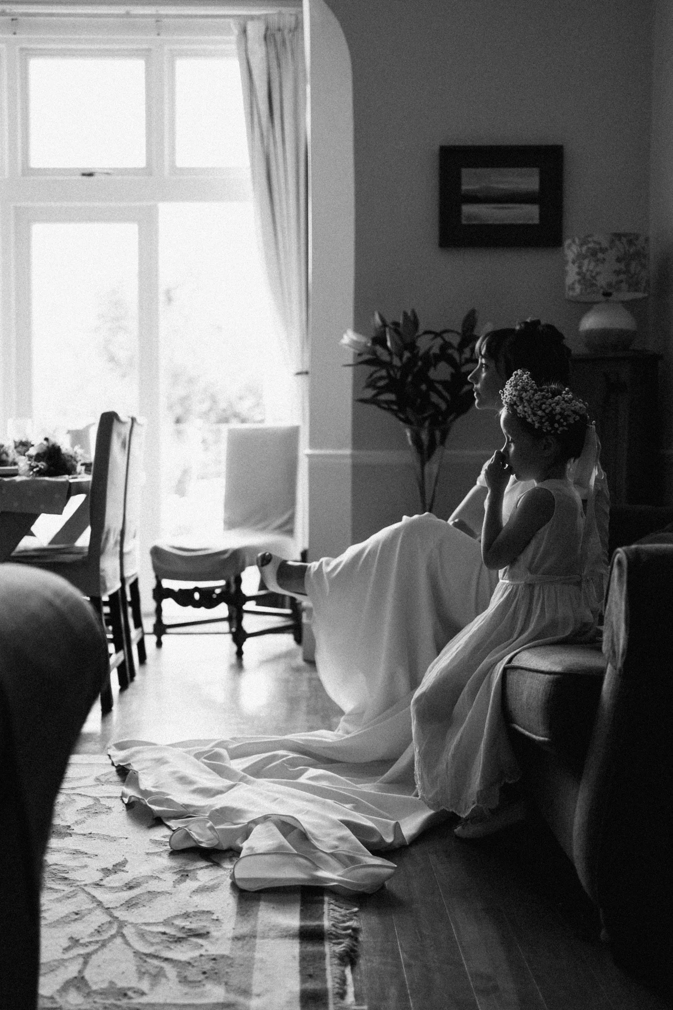 Bride and flower girl sitting on a sofa in beautiful natural light, waiting to leave for the ceremony