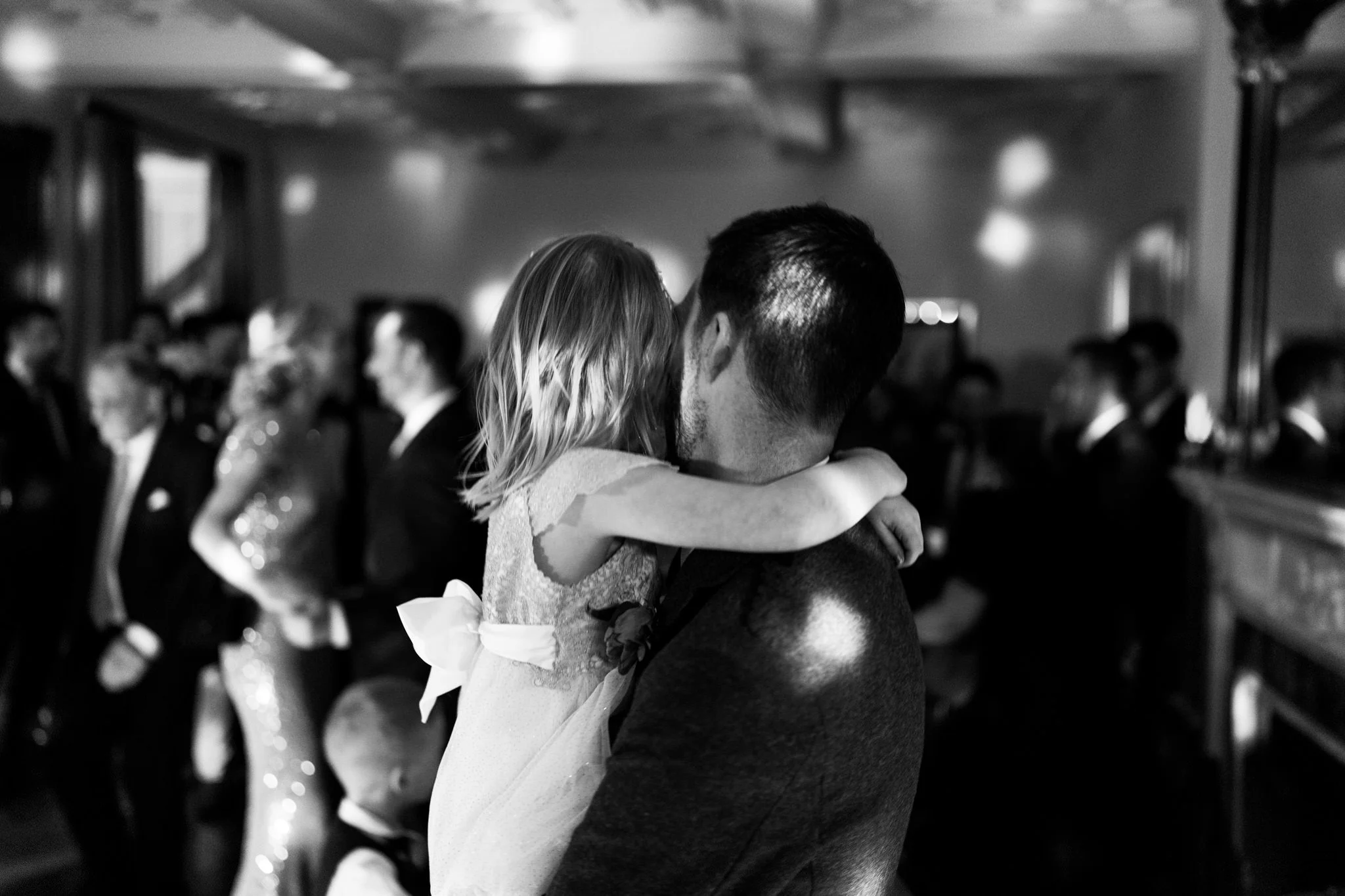 Man and young daughter watching the dancing at a wedding, she has her arms round his neck