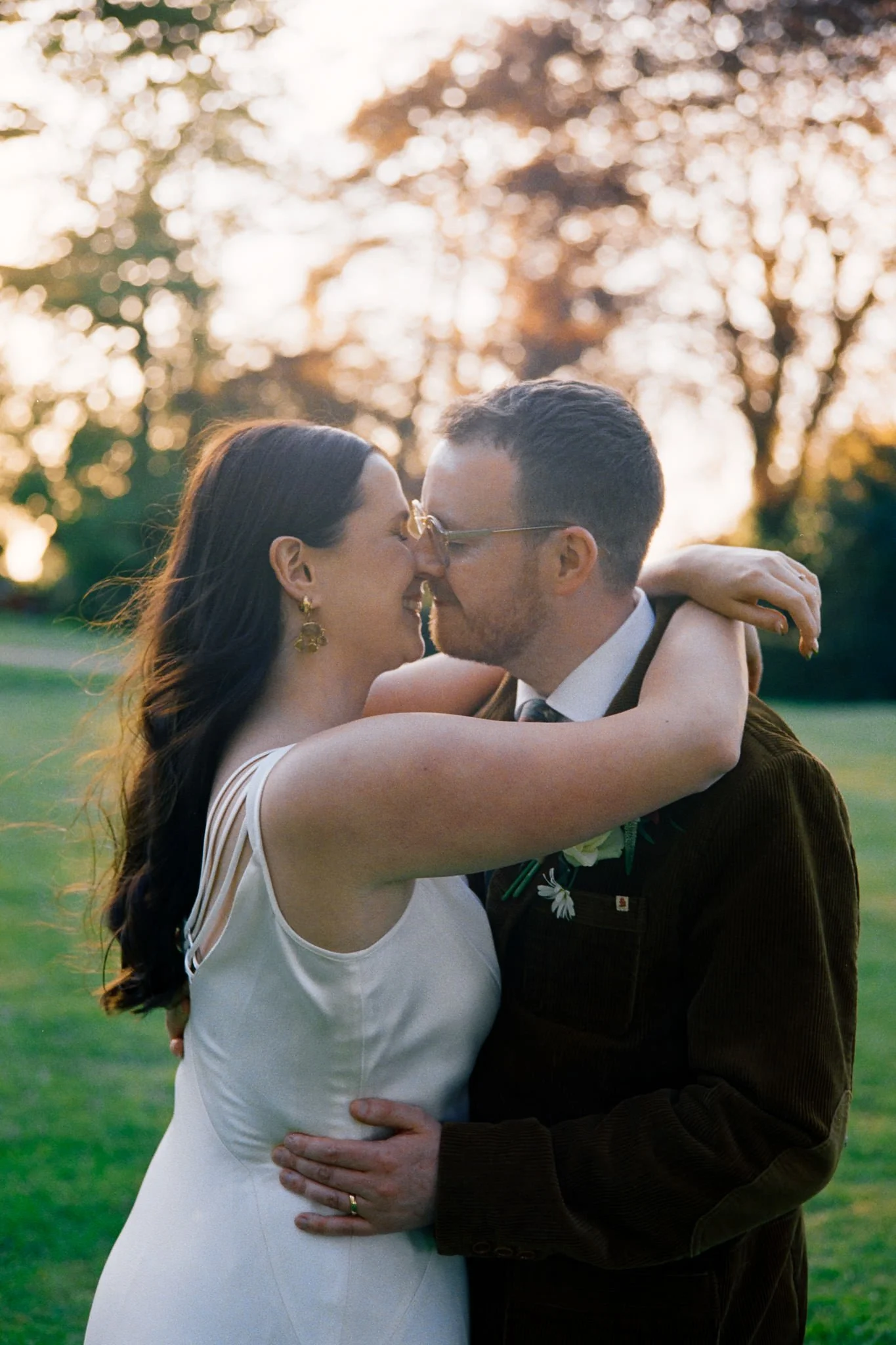 Bride and groom embrace in sunset dappled trees at their wedding