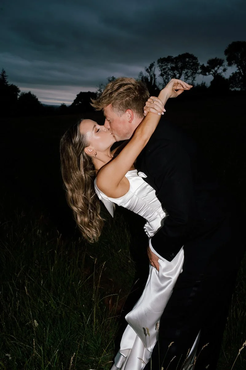 Bristol wedding photographer captures a couple in a dramatic dip-and-kiss, lit by flash against a dark evening backdrop — bold, colour reportage-style wedding photography