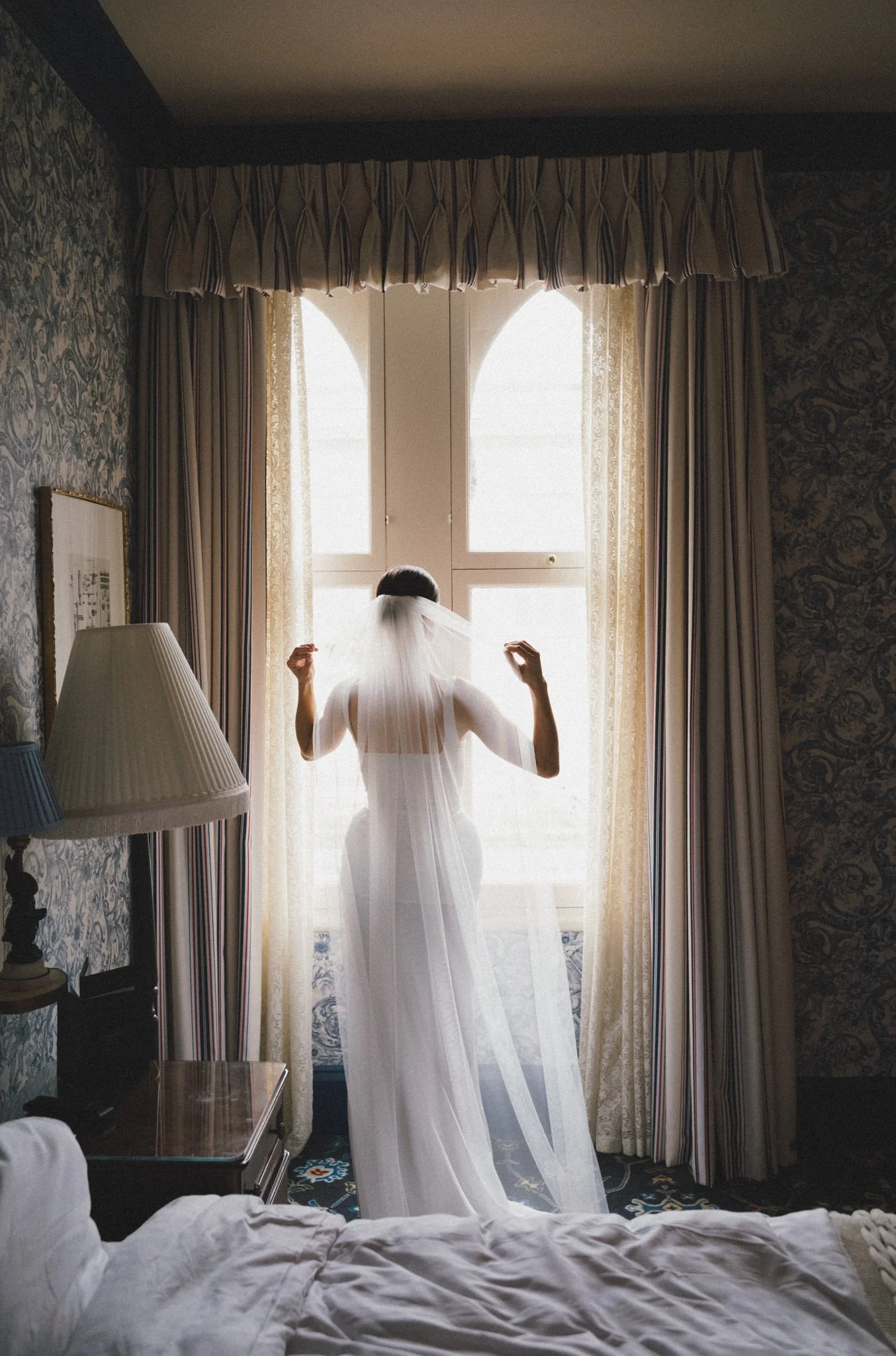 wedding photography of a bride adjusting her veil by a window at the Randolph Hotel in Oxford