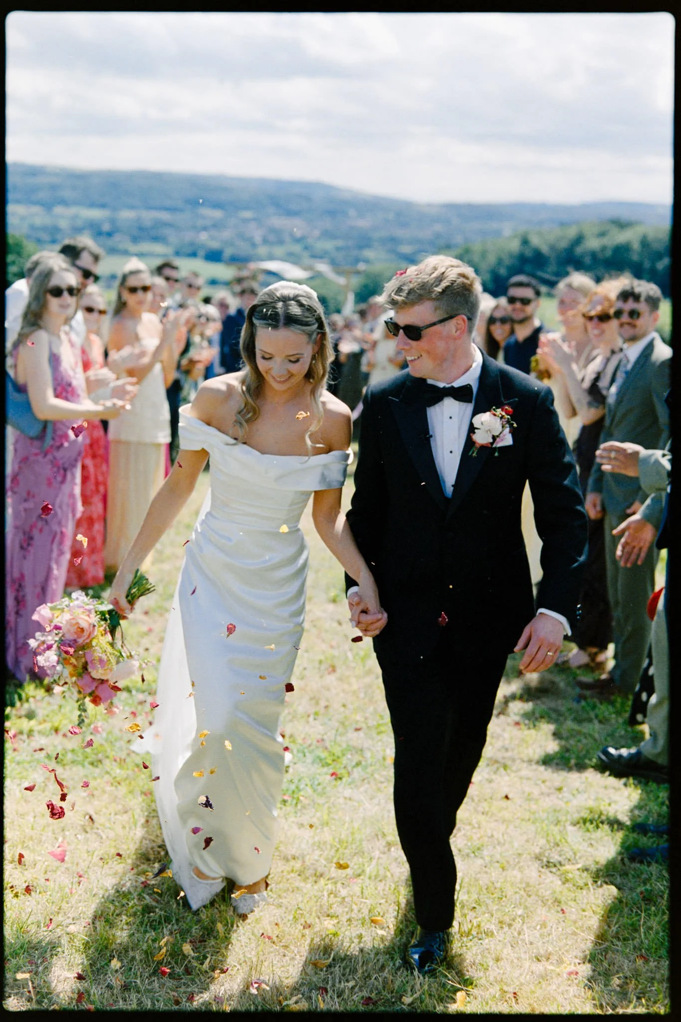 Bride and groom confetti walk in a field in Somerset, shot on Kodak portra 400 film with a shallow depth of field.