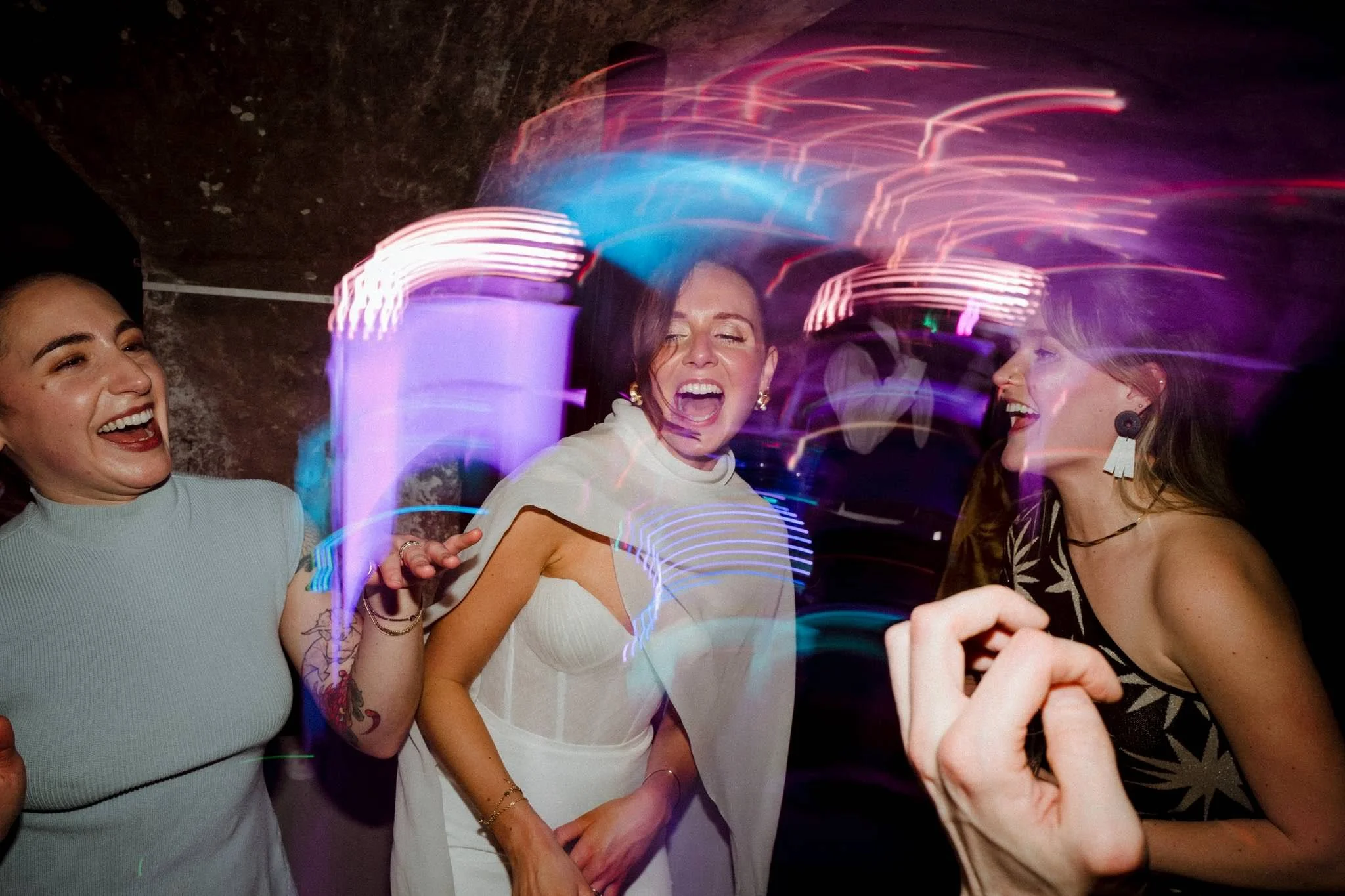 Three women laughing and enjoying themselves at a party with colorful, blurred lights in the background.