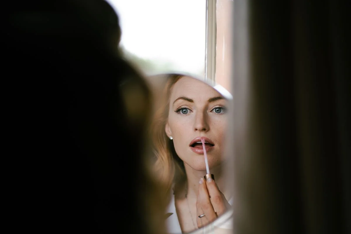 Bride applies lipstick in the mirror during wedding morning prep, captured in natural colour light by a Bristol documentary wedding photographer