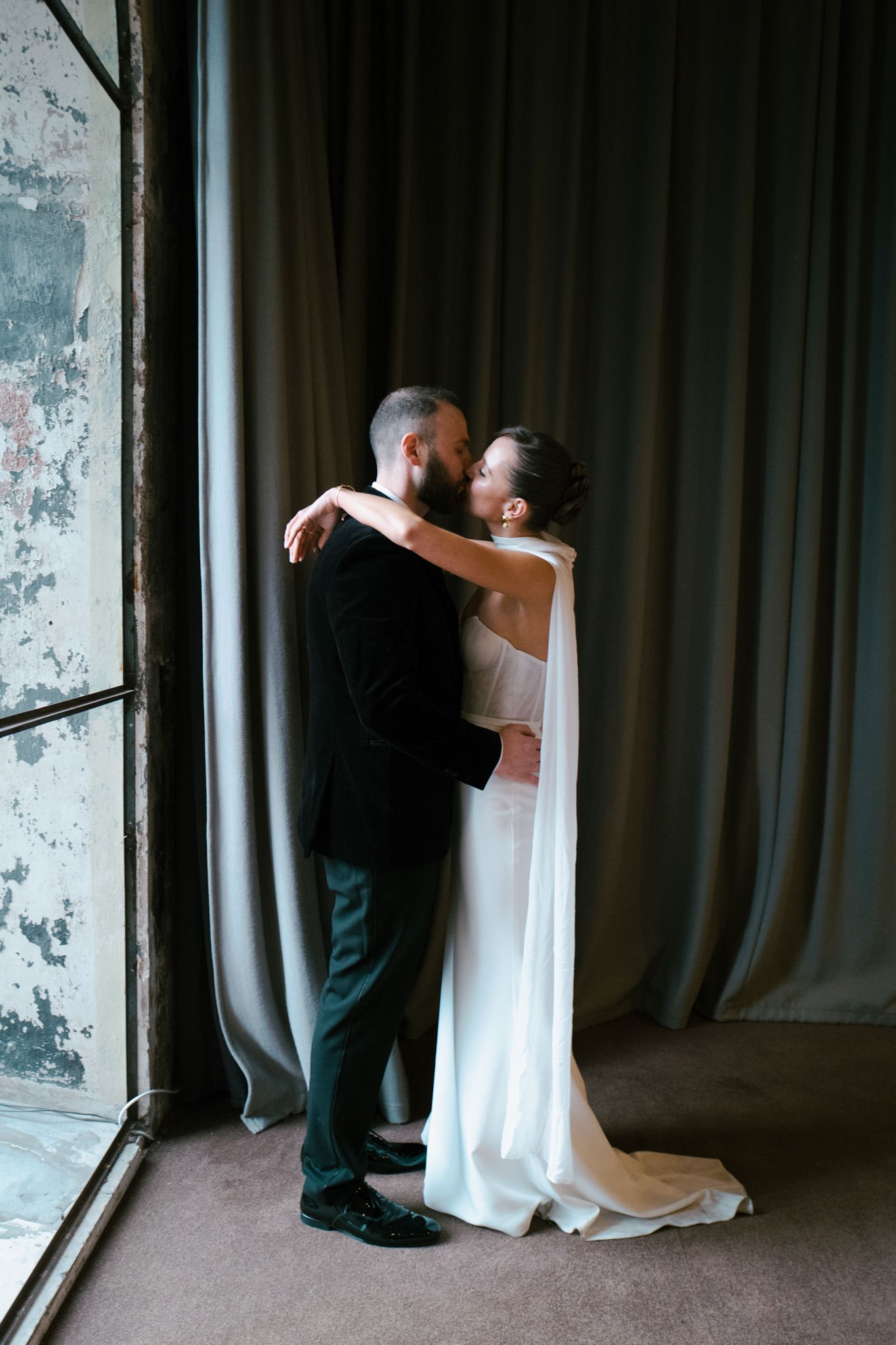Newlyweds kissing at the mount without in Bristol by a big window on a rainy day