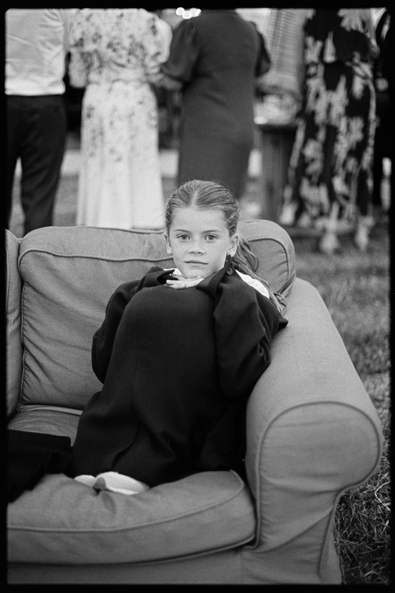 Young girl sitting on a sofa at a wedding near Bristol with a  very mature stare at the camera, shot in black and white Tri-x film