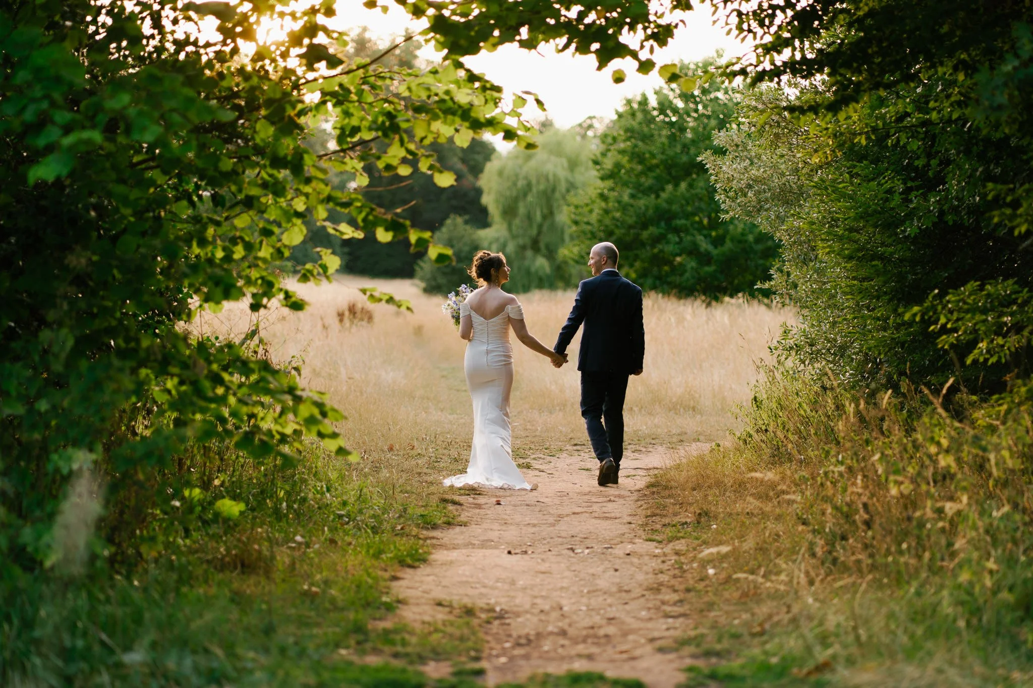 Bride and groom at sunset in Bristol walking down a path between trees and bushes