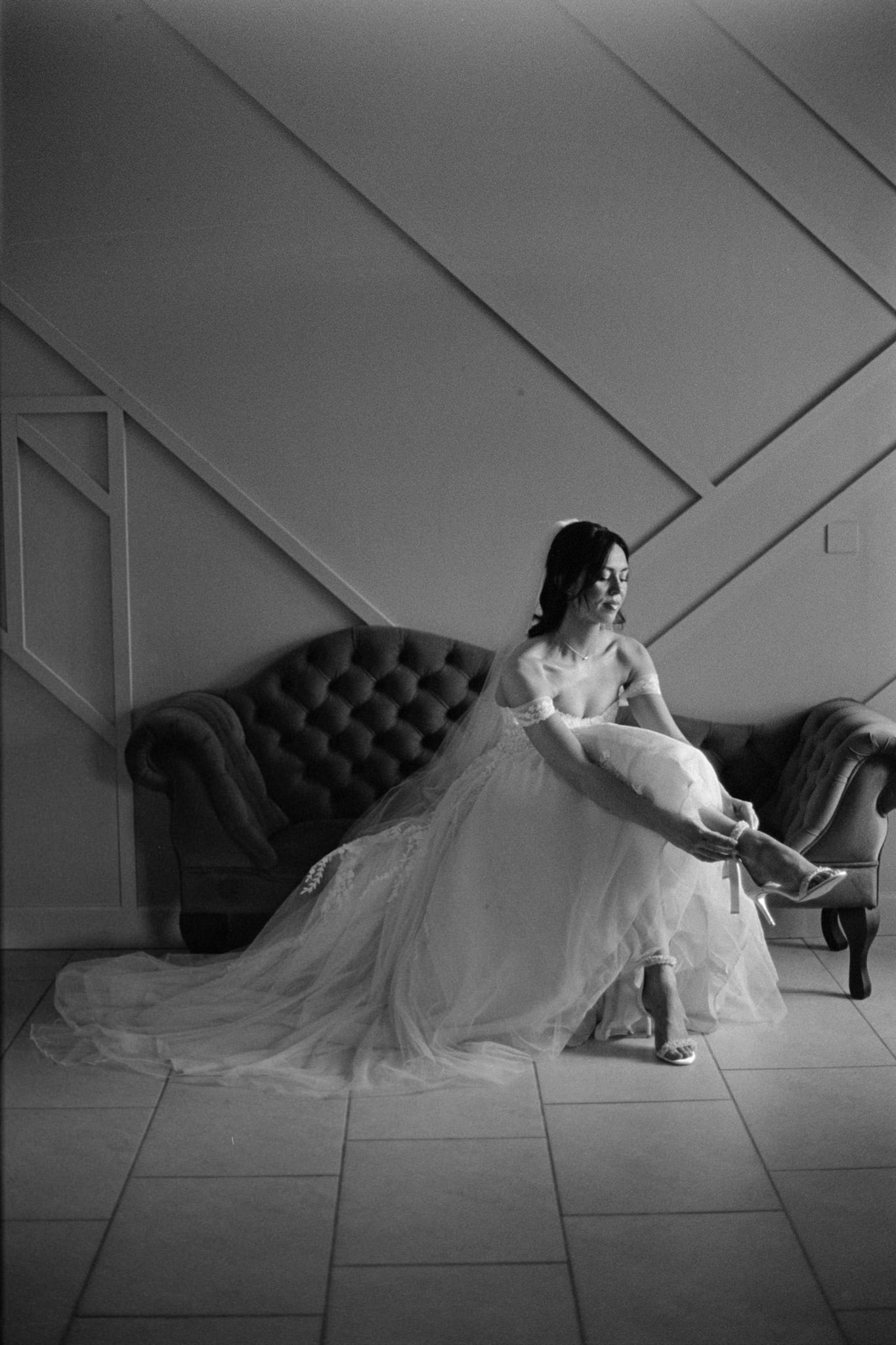 wedding photography of a bride putting her shoes on whilst sitting on a couch at Kingscote Barn