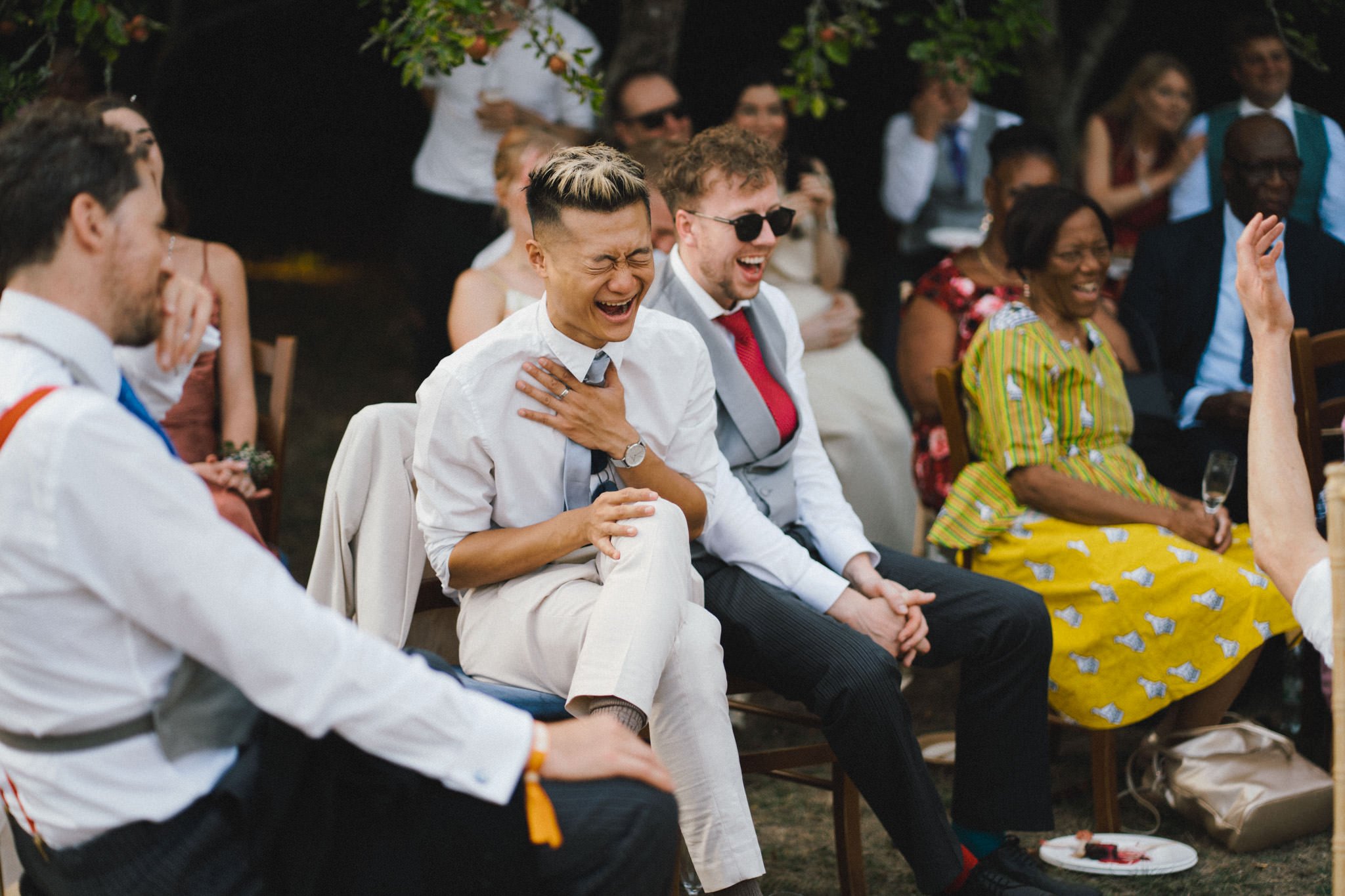 wedding photography of an asian male guest laughing during speeches