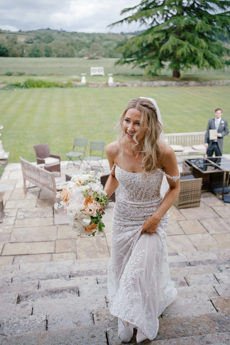 Bride in a delicate lace gown climbs the stone steps at Llangoed Hall — a candid colour wedding portrait in natural light